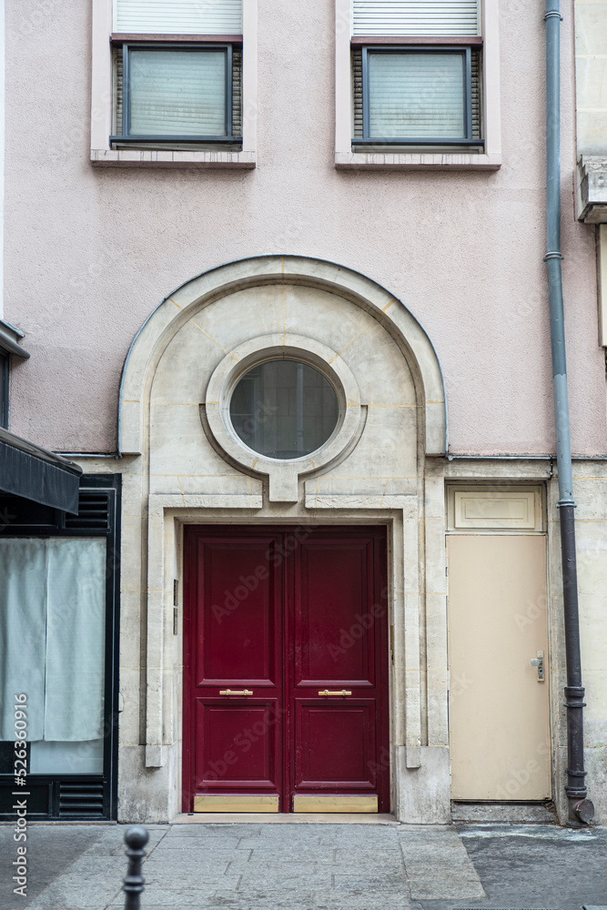Close-up of a vintage red front door of a building in Paris, with a stone arch above