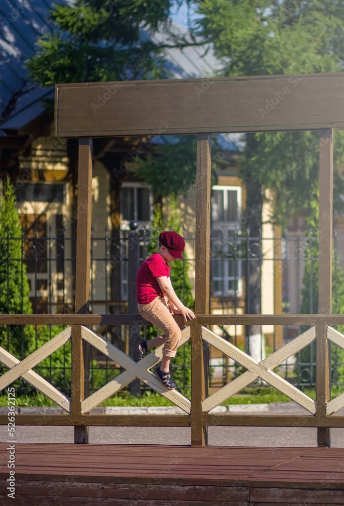 A 9-year-old white boy in a cap is sitting on the fence