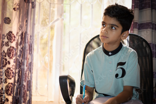 A young boy is thinking while writing a story