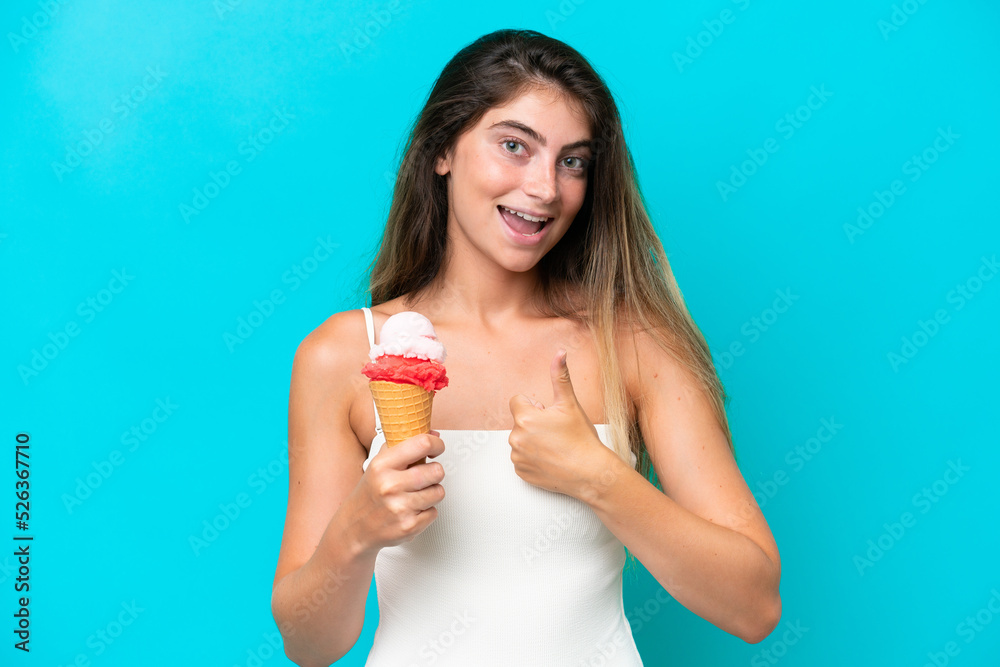 Young woman in swimsuit holding an ice cream isolated on blue background with thumbs up because something good has happened Young woman in swimsuit holding an ice cream isolated on blue background with thumbs up because something good has happened