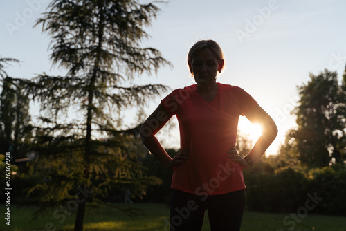 Mature woman silhouette doing sports outdoors on a sunset summer day in park