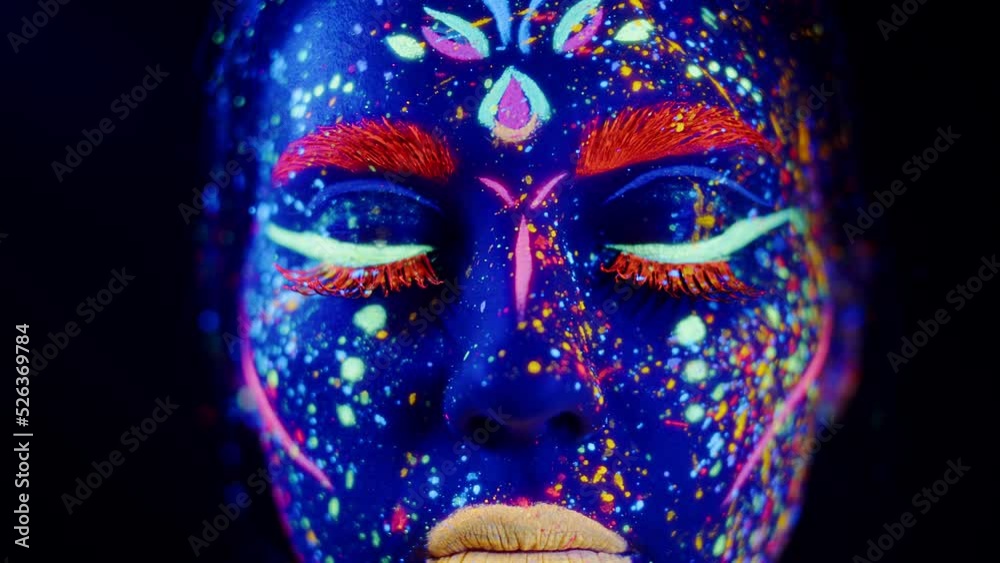 Closeup portrait of an attractive young girl in bright blacklight bodyart, neon party makeup, blinking her eyes. Studio shot in darkness Closeup portrait of an attractive young girl in bright blacklight bodyart, neon party makeup, blinking her eyes. Studio shot in darkness