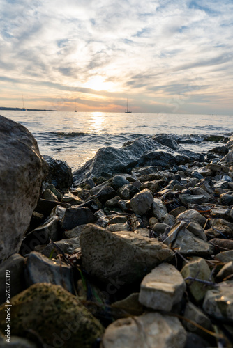 Sonnenuntergang am Meer mit Segelbooten im Hintergrund und Steinen im Vordergrund