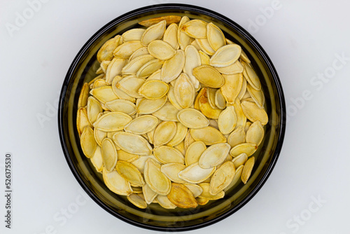 фотографія Dried pumpkin seeds in husks in a black bowl on a white background