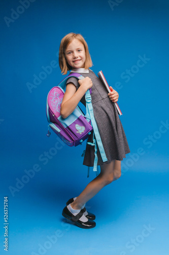 Back to school. A schoolgirl with a school bag on an isolated blue studio background. a little girl is holding a backpack.