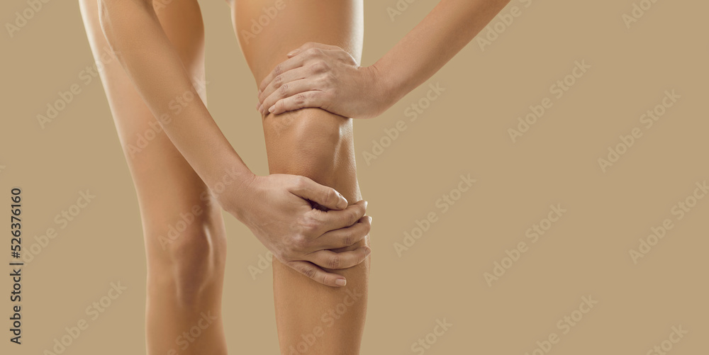 Narrow show crop closeup image of woman on yellow background suffer from knee ache. Acute pain in kneecap. Unhealthy female touch leg having arthritis or osteoporosis. Healthcare problem.