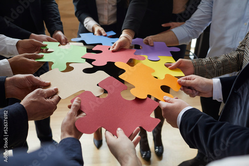 Business team trying to find creative solutions to problem. Group of people connecting different red, yellow, orange, green, blue and purple jigsaw puzzle pieces. Cropped close up. Teamwork concept