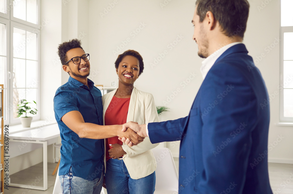 Obraz premium Black couple shaking hands with loan broker. Happy family meeting with realtor or real estate agency representative to establish good, successful partnership relations and confirm future collaboration