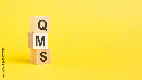 QMS - Quality Management System - text on wooden block with yellow background. photo