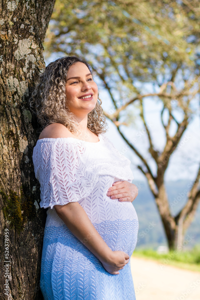 vertical photo pregnant woman in white dress leaning against the tree. vertical photo pregnant woman in white dress leaning against the tree.
