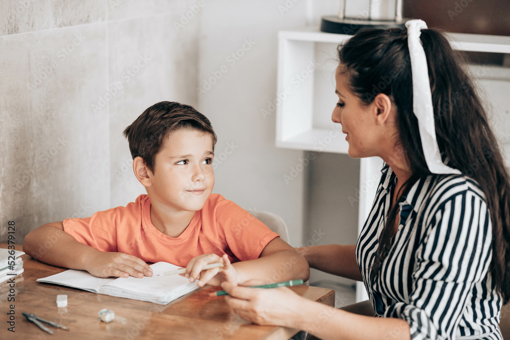 Little school boy doing homework with his mom helping him with assignments Little school boy doing homework with his mom helping him with assignments