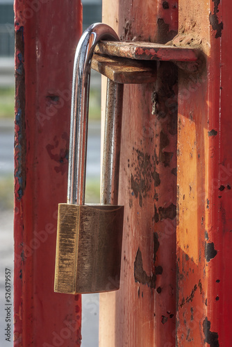 Old worn padlock locked on the paint-shabby gate. Metaphor of a liquidated business. Soft focus view.