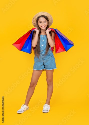 happy teen child with purchase bags on yellow background. full length