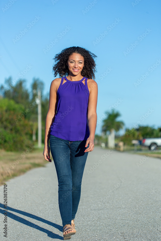 Beautiful young black African American woman walking down the street toward the viewer or camera with a smile