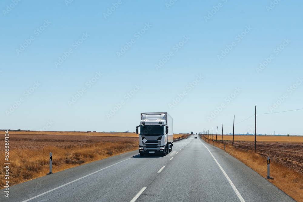 Refrigerator truck driving on a straight road, with a flat horizon and a clear sky.