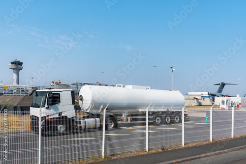 Aviation fuel tanker unloading at an airport facility, with the control tower and an airplane in the background.