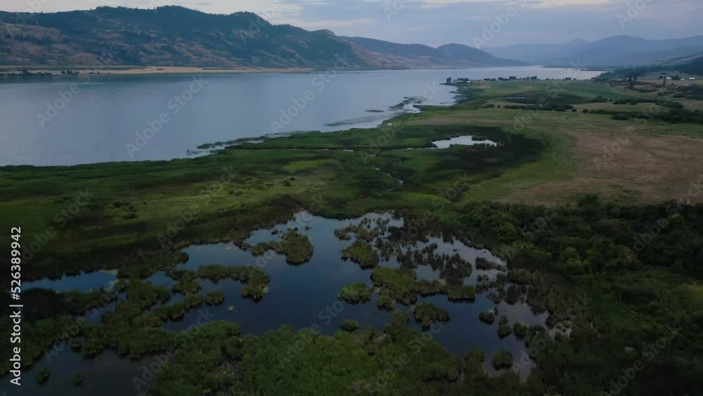 Aerial View of Okanagan Lake with farm lands and mountain landscape. Cloudy Sunset Sky. Near Vernon, British Columbia, Canada. Aerial View of Okanagan Lake with farm lands and mountain landscape. Cloudy Sunset Sky. Near Vernon, British Columbia, Canada.