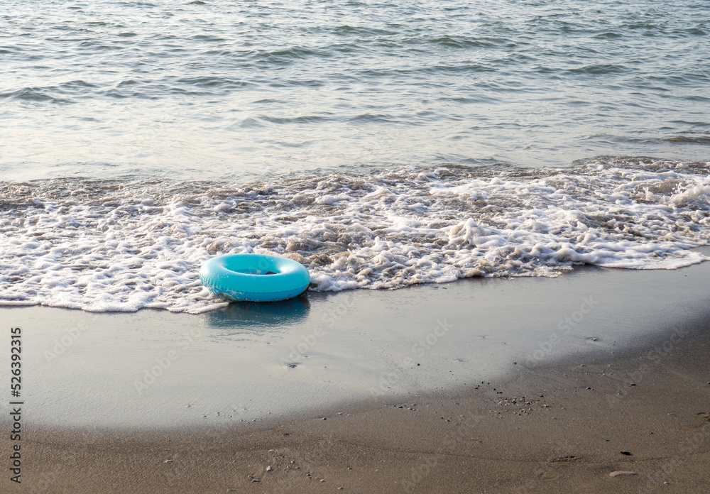 The swimming ring is carried by the wave. Inflatable circle on the beach. Black sand on the beach. The swimming ring is carried by the wave. Inflatable circle on the beach. Black sand on the beach.