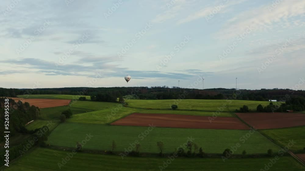 Drone shot, view of a hot air balloon in the sky flying over green fields on a sunny day, Germany. Drone shot, view of a hot air balloon in the sky flying over green fields on a sunny day, Germany.