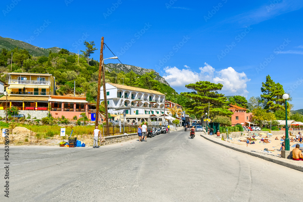 The sandy beach, cafes ans shops at the colorful seaside town of Palaiokastritsa, Greece, on the island of Corfu.