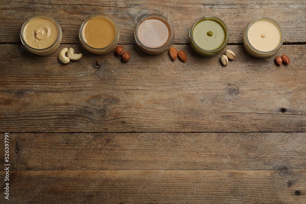 Jars with butters made of different nuts and ingredients on wooden table, flat lay. Space for text Jars with butters made of different nuts and ingredients on wooden table, flat lay. Space for text