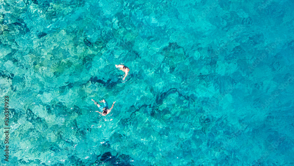 Drone photo of a people enjoying a swim in the turquoise sea at the remote beach surrounded by the cliffs in the Turkish Riviera