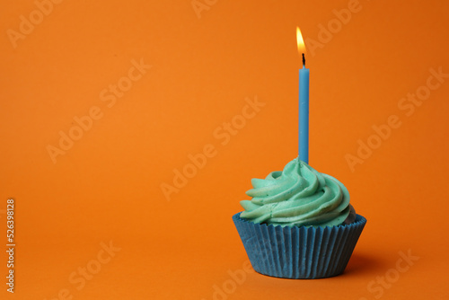 Delicious birthday cupcake with turquoise cream and burning candle on orange background. Space for text