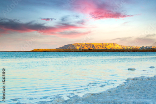 Dead Sea coastline, evening sun shines on salt crystals formations, clear water mountains at sunset time. Picture at Dead Sea beach in Ein Bokek. Waterscape of seashore. Beautiful nature landscape