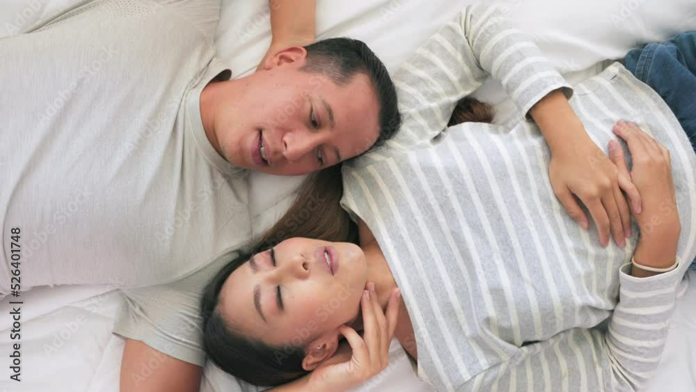 The Close-up of the Asian couple is Lying happily chatting in bed together. They meet each other's eyes showing love. Top view The Close-up of the Asian couple is Lying happily chatting in bed together. They meet each other's eyes showing love. Top view