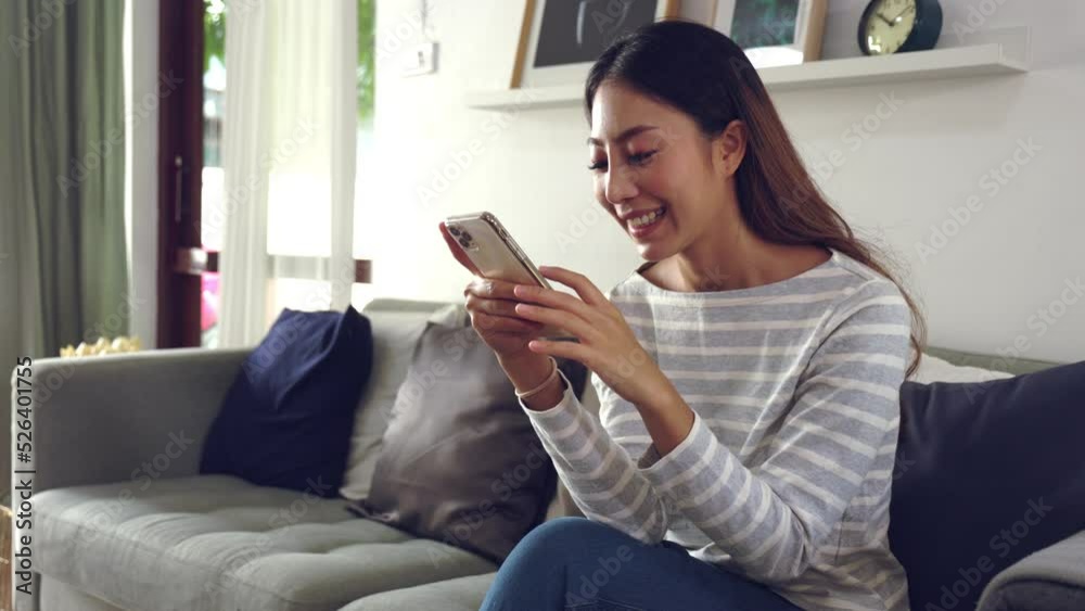 slow motion shot. an Asian Young woman watching online content on a smartphone and shopping online. Her sitting on a sofa at home in the living room slow motion shot. an Asian Young woman watching online content on a smartphone and shopping online. Her sitting on a sofa at home in the living room