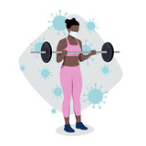 Ćwiczenia z maską na twarzy. Kobieta trenująca ramiona ze sztangą na siłowni w masce medycznej chroniącej przed wirusem Covid-19. Sport podczas pandemii koronawirusa.