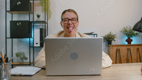 Obraz na płótnie Business woman hiding behind laptop computer, making funny face, fooling around, putting his tongue out remote working disrespecting someone at home office