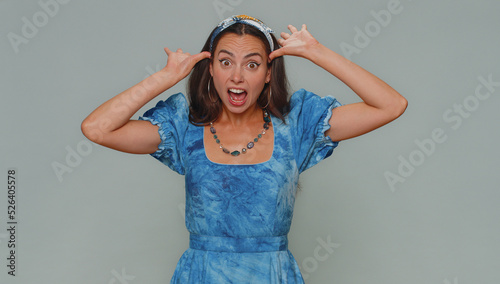 Lovely pretty funny woman in dress making playful silly facial expressions and grimacing, fooling around, showing tongue. Adult stylish female girl isolated alone on gray studio background indoors