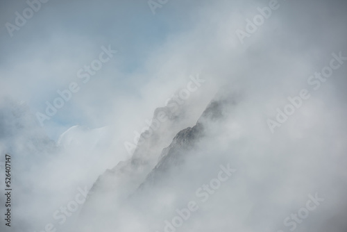 Lovely scenery with big snowy mountains in thick clouds. High mountain wall in gantly cloudy sky. Scenic view to large snow mountain in clearance of dense fog. Beautiful diagonal rocks in low clouds.