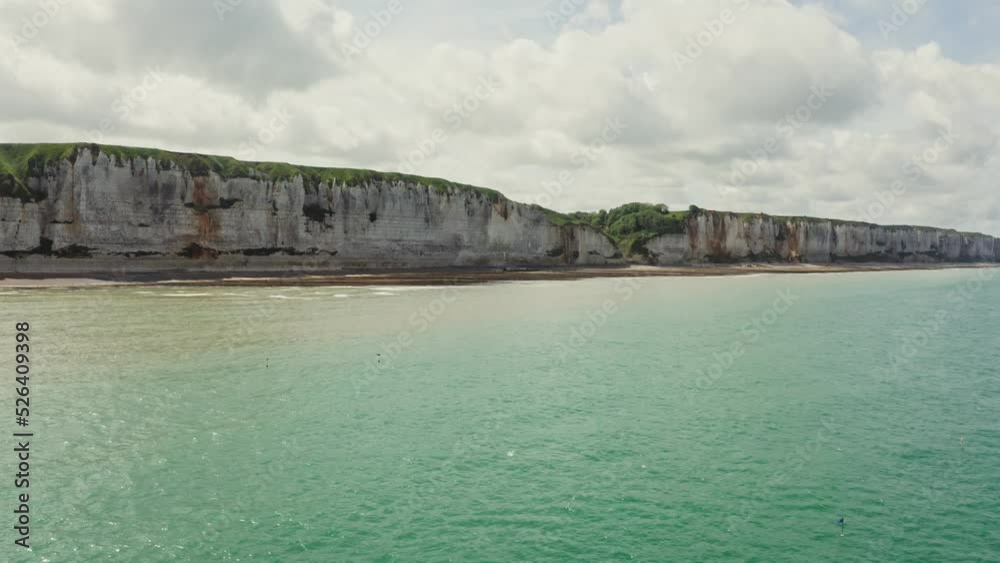 A sandy beach without people at the foot of striped limestone cliffs with bizarre peaks covered with thick green grass. Etretat, France A sandy beach without people at the foot of striped limestone cliffs with bizarre peaks covered with thick green grass. Etretat, France