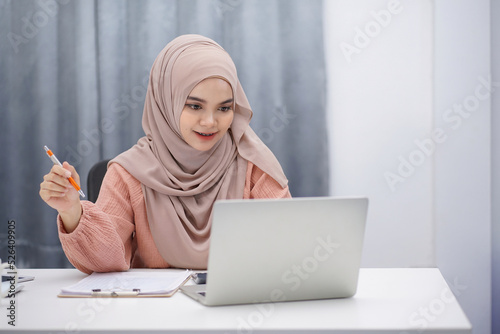 Happy asian muslim woman brown hijab working at home with laptop and documents.