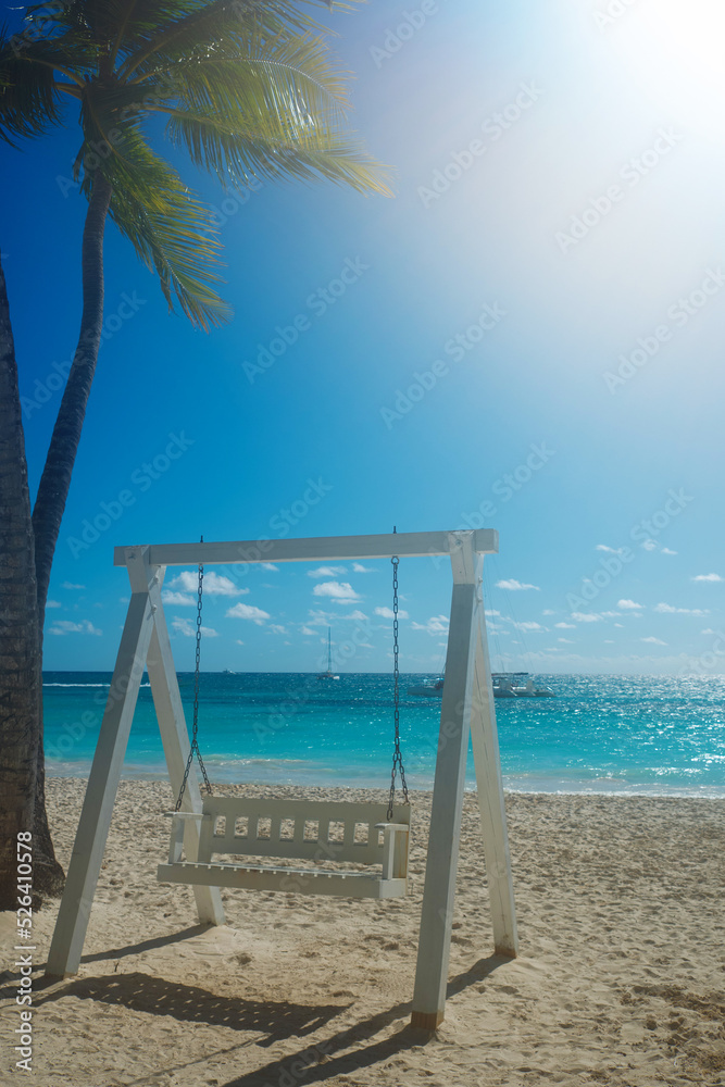 Dominican Republic, a beautiful beach with white sand and azure ocean. White beautiful swing for relaxing on the shore Dominican Republic, a beautiful beach with white sand and azure ocean. White beautiful swing for relaxing on the shore
