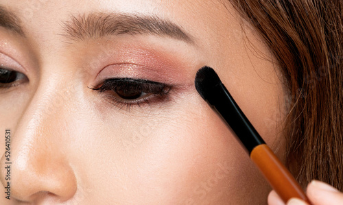 Closeup ardent young woman with healthy fair skin applying her eyeshadow with brush. Female model with fashion makeup. Beauty and makeup concept. photo