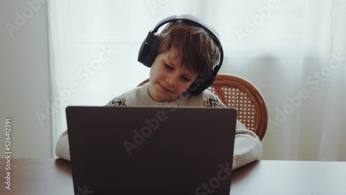 Caucasian kid boy wearing headphones studying online from home
