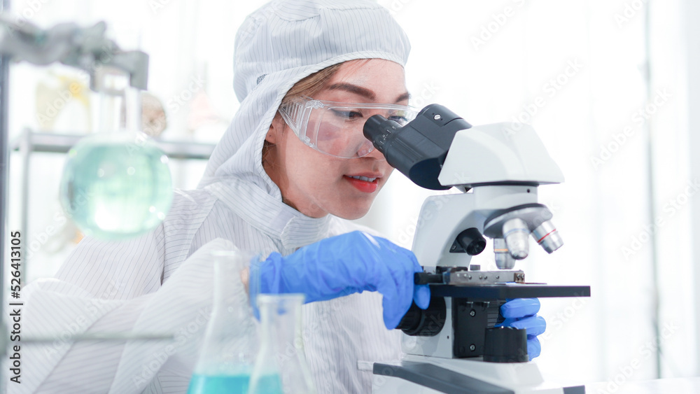 beautiful Asian woman researcher wearing protective clothing and glasses uses microscope while studying the virus in the laboratory. beautiful Asian woman researcher wearing protective clothing and glasses uses microscope while studying the virus in the laboratory.