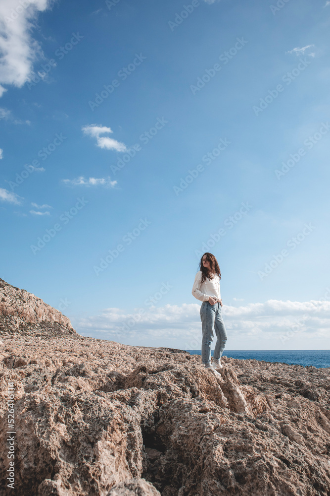 Young woman is standing in a desert ground in front of the mountain Cape Greco