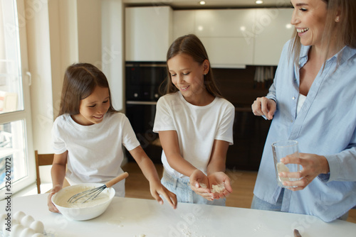 Happy family preparing food together in the kitchen. Mom teaches her daughters how to cook and knead the dough. Mother's Day concept. playing with flour
