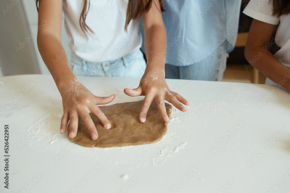 two little girls and their beautiful mother in aprons play and laugh while kneading dough in the kitchen. bake gingerbread cookies