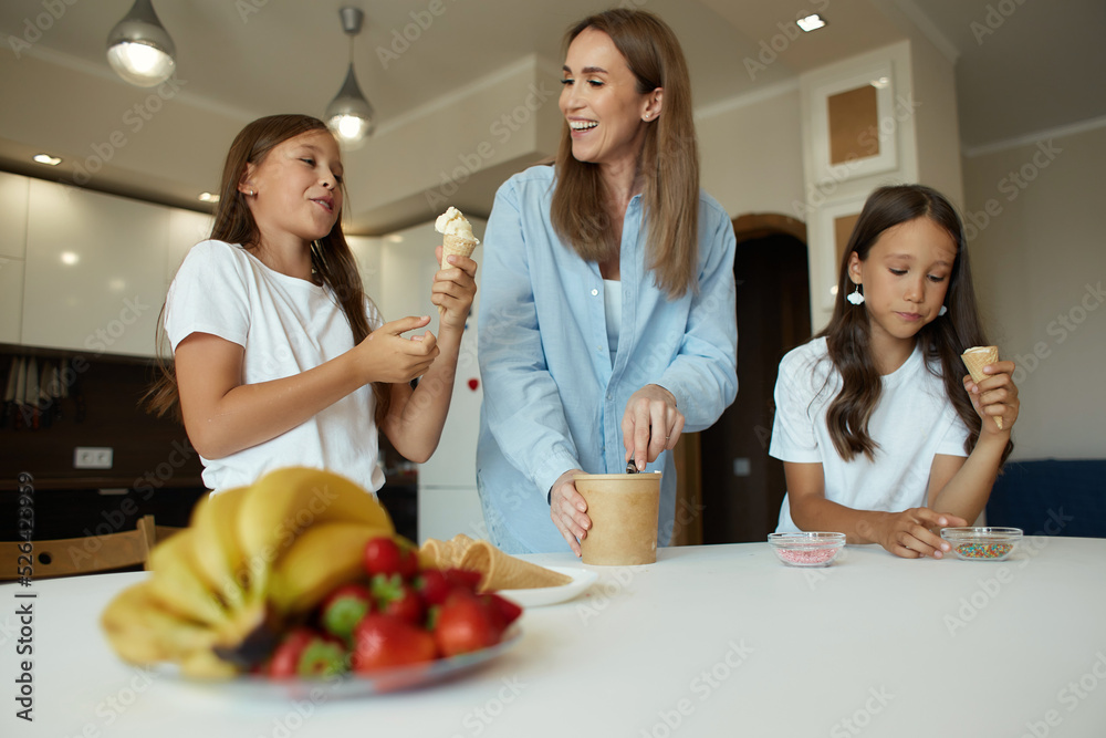 Young beautiful mother and her daughters have fun together. A beautiful woman and her little children are preparing ice cream. Family having fun eating ice cream balls