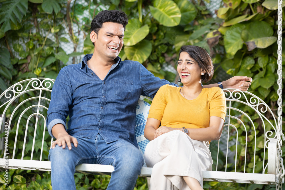 Happy young indian couple pending time together while sitting on hanging swing. Happy young indian couple pending time together while sitting on hanging swing.