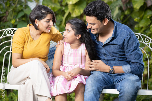 Happy young indian family spending time together while sitting on hanging swing. parents with daughter.