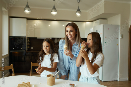Young beautiful mother and her daughters have fun together. A beautiful woman and her little children are preparing ice cream. Family having fun, eating ice cream balls, stained with cream