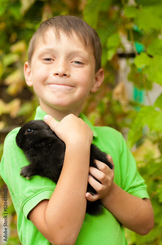 A cute boy in a green t-shirt holds a rabbit in his arms in nature in summer. Animals and children A cute boy in a green t-shirt holds a rabbit in his arms in nature in summer. Animals and children