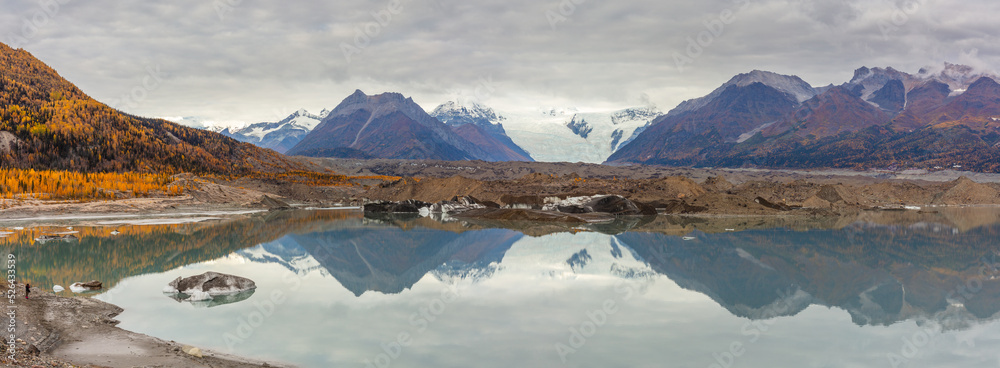 Panorama of a mountain landscape with the debris covered terminus of a huge glacier reflecting in a glacial lake