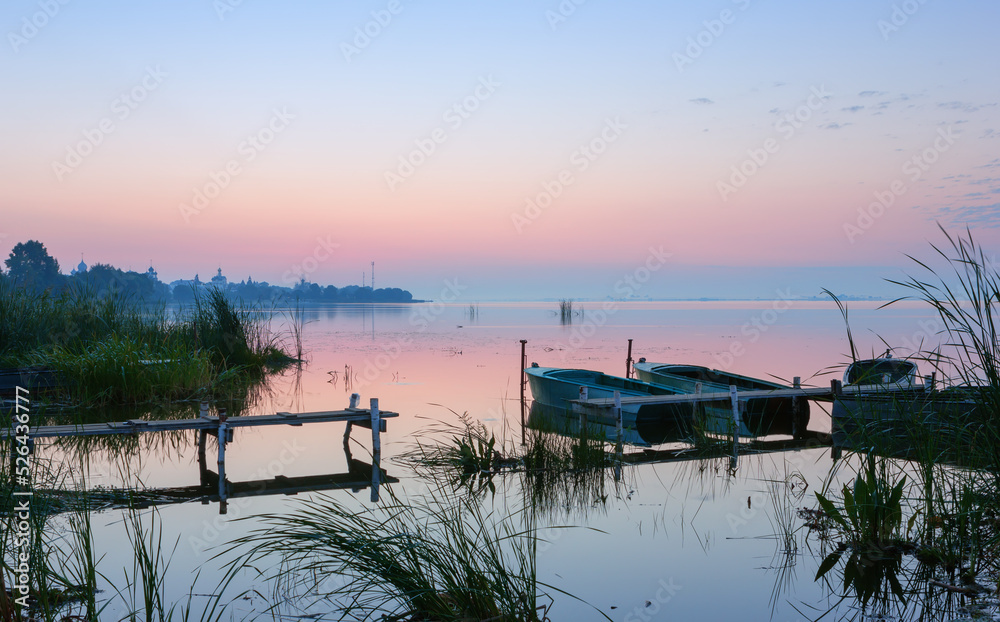 Gentle Pink-Blue Dawn Before Sunrise Over the Overgrown Shore of a Calm Lake with Moored Boats. Lake Nero, Rostov Veliky, Russia.